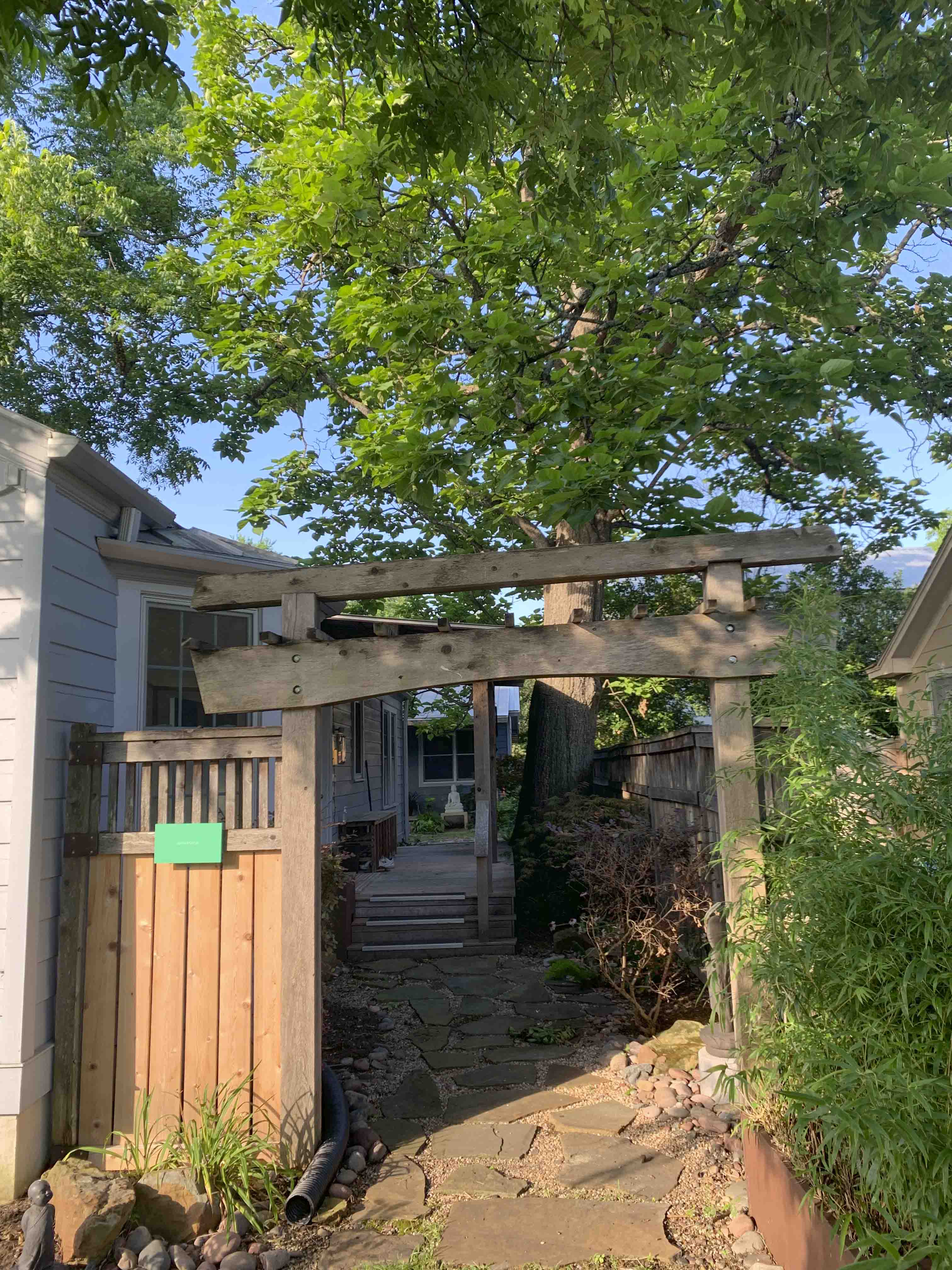 The garden gate at Appamada — a wooden arbor entrance with stone path leading to the practice space