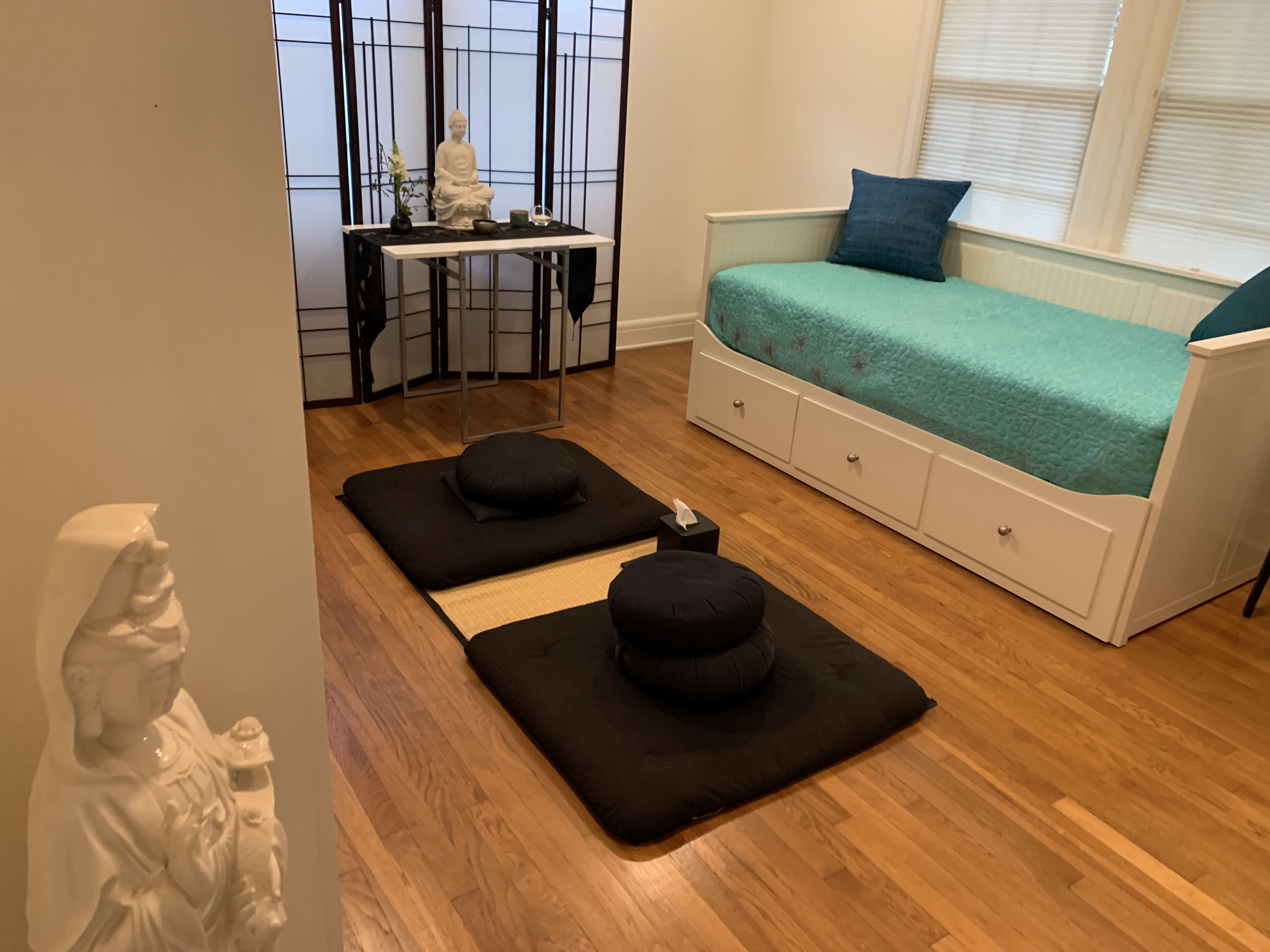 A practice room at Appamada — zafu and zabuton cushions on hardwood floor, Buddha statue, and shoji screen